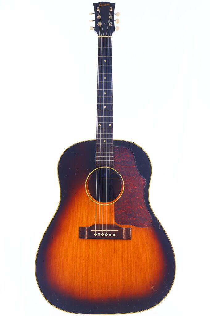 Die Gibson J-45 1957 Akustik Gitarre Hat Ein Sunburst-Finish Mit Dunklen Rändern, Die In Eine Warme Bernsteinfarbene Mitte Übergehen, Ein Schildpatt-Schlagbrett, Sechs Saiten Und Weiße Wirbel, Die Vor Einem Weißen Hintergrund Abgebildet Sind.
