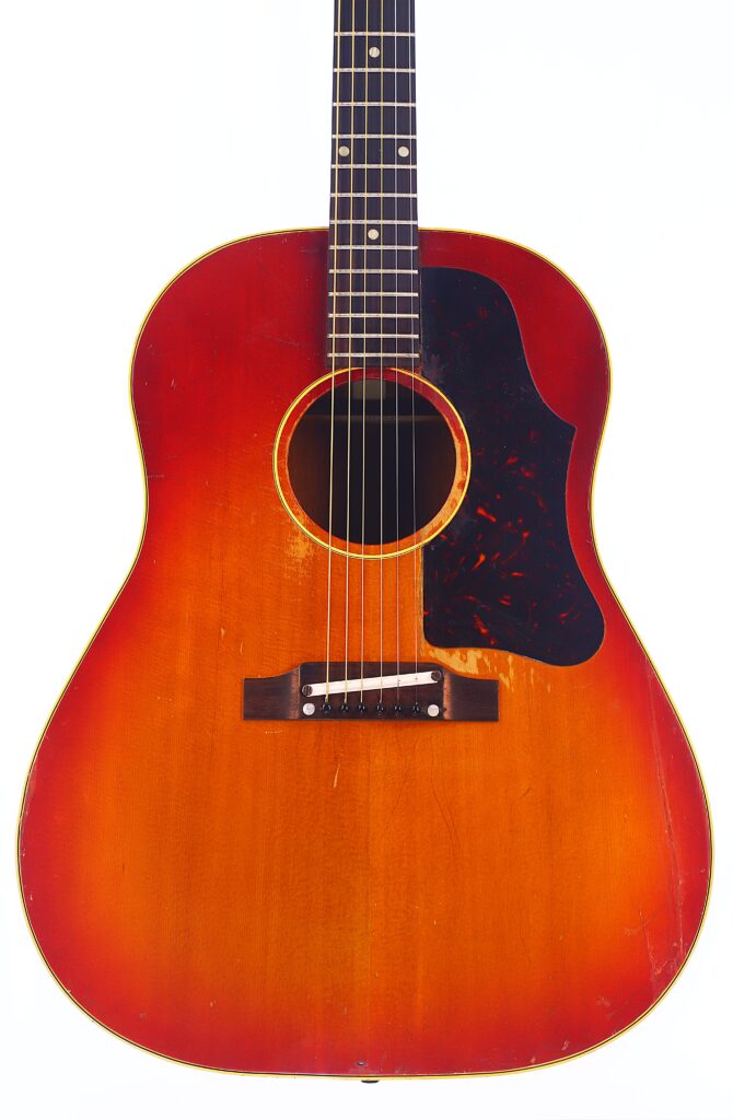 Eine Gibson J-45 1962 Akustik-Gitarre Mit Sunburst-Lackierung, Schildpatt-Schlagbrett, Sechs Saiten Und Sichtbaren Gebrauchsspuren Wird Vom Hals Bis Zum Korpus Auf Weißem Grund Gezeigt.