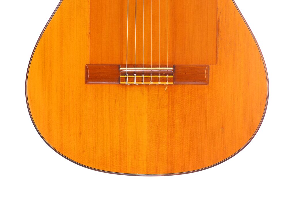 Nahaufnahme Der Unteren Hälfte Einer Lester Devoe 1996 Negra Flamenco Gitarre, Wobei Die Saiten, Der Steg Und Der Glatte Hellbraune Holzkorpus Hervorgehoben Werden.