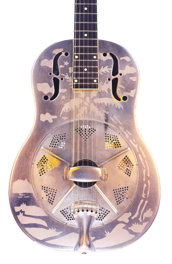 Eine Nahaufnahme Der National Reso-Phonic Style O 2009 Akustik Gitarre, Die Sich Durch Eine Metallkonstruktion Mit Eingravierten Motiven Und Zwei F-Löchern Auszeichnet, Fotografiert Vor Einem Weißen Hintergrund.