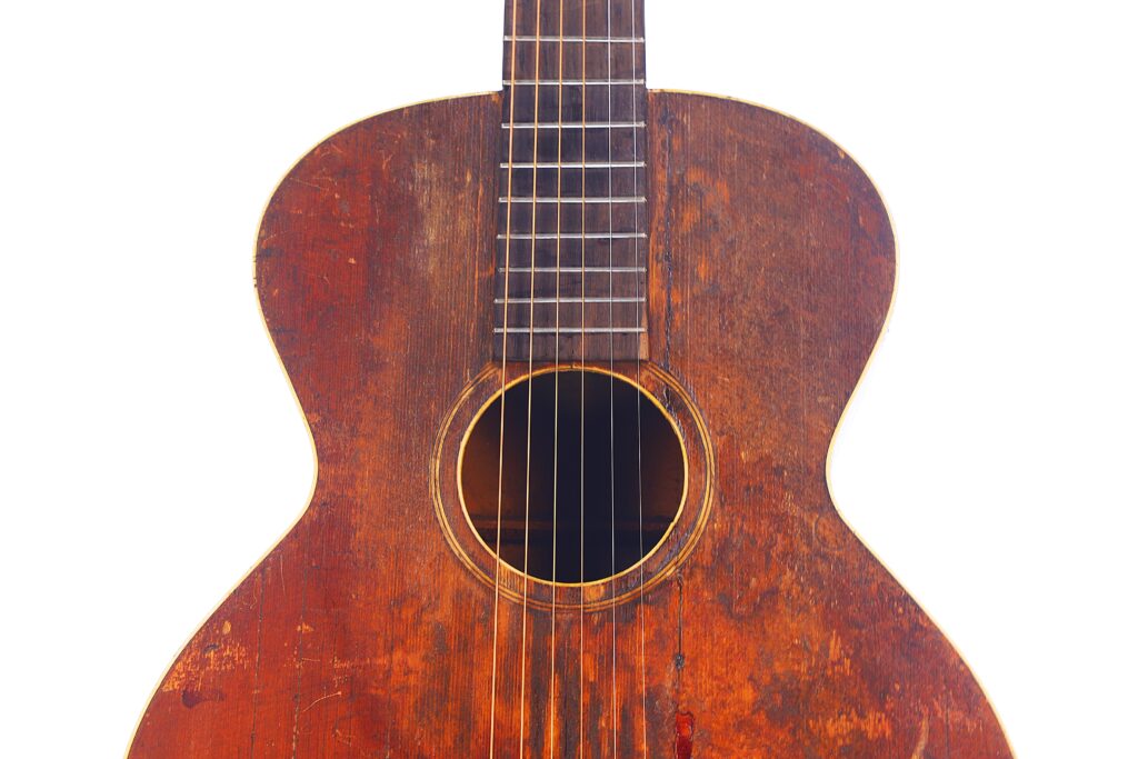 Nahaufnahme Des Korpus Und Der Saiten Der Gibson L-1 1926 Akustikgitarre, Die Die Rotbraune, Zerkratzte Holzoberfläche Auf Weißem Hintergrund Zeigt.