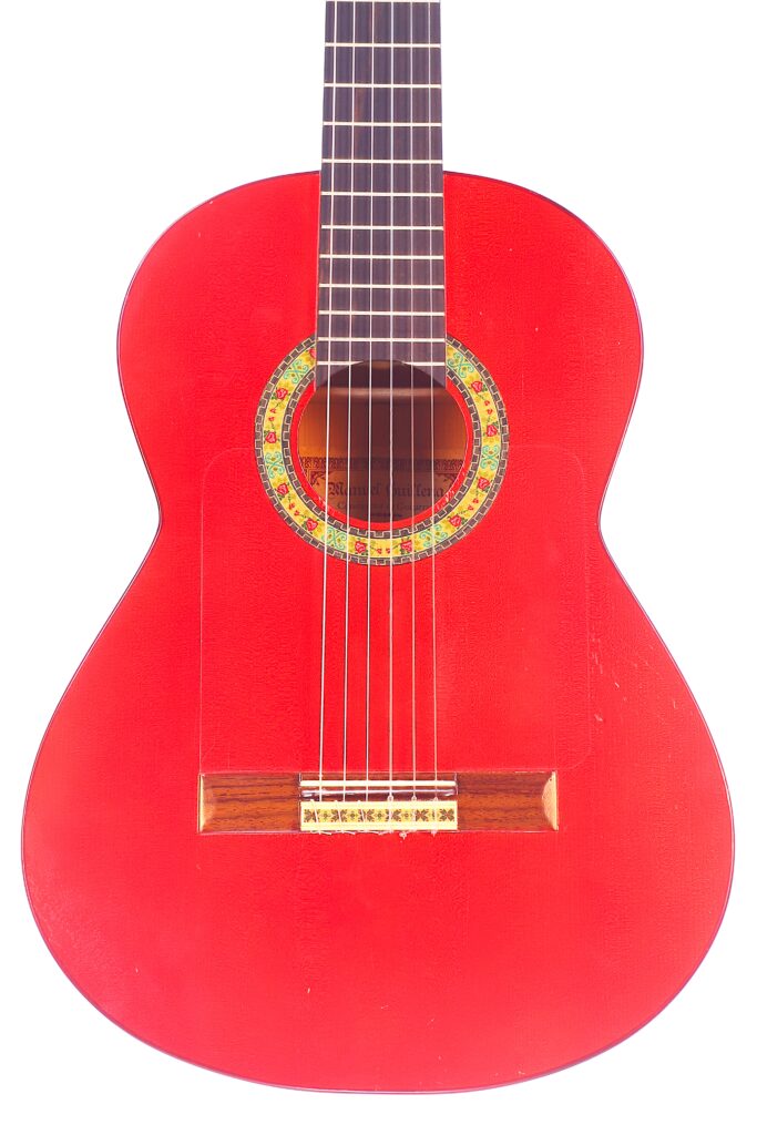 Die Manuel Guillena 2017 Blanca Flamenco Gitarre Ist Eine Leuchtend Rote Klassische Akustikgitarre Mit Sechs Saiten, Einer Dekorativen Rosette Um Das Schallloch Und Einem Holzsteg, Abgebildet Vor Einem Weißen Hintergrund.