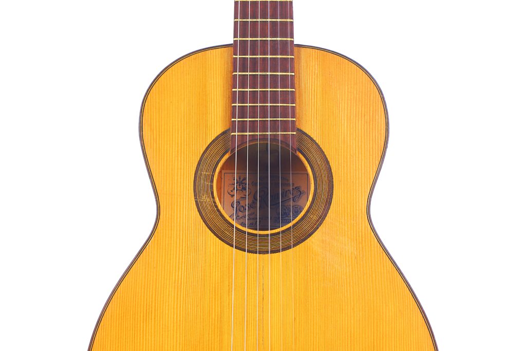 特写何塞-拉米雷斯创作于 1953 年的弗拉门戈吉他,木制琴身、音孔和部分琴颈,白色背景下有六根弦和音格。.