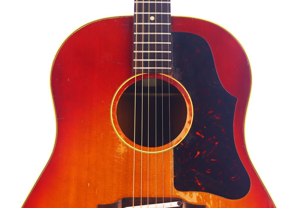 Nahaufnahme Des Korpus Einer Gibson J-45 1962 Akustik Gitarre Mit Rötlich-Braunem Finish, Sichtbaren Kratzern Und Abnutzungserscheinungen, Schwarzem Schlagbrett Und Sechs Saiten Vor Weißem Hintergrund.