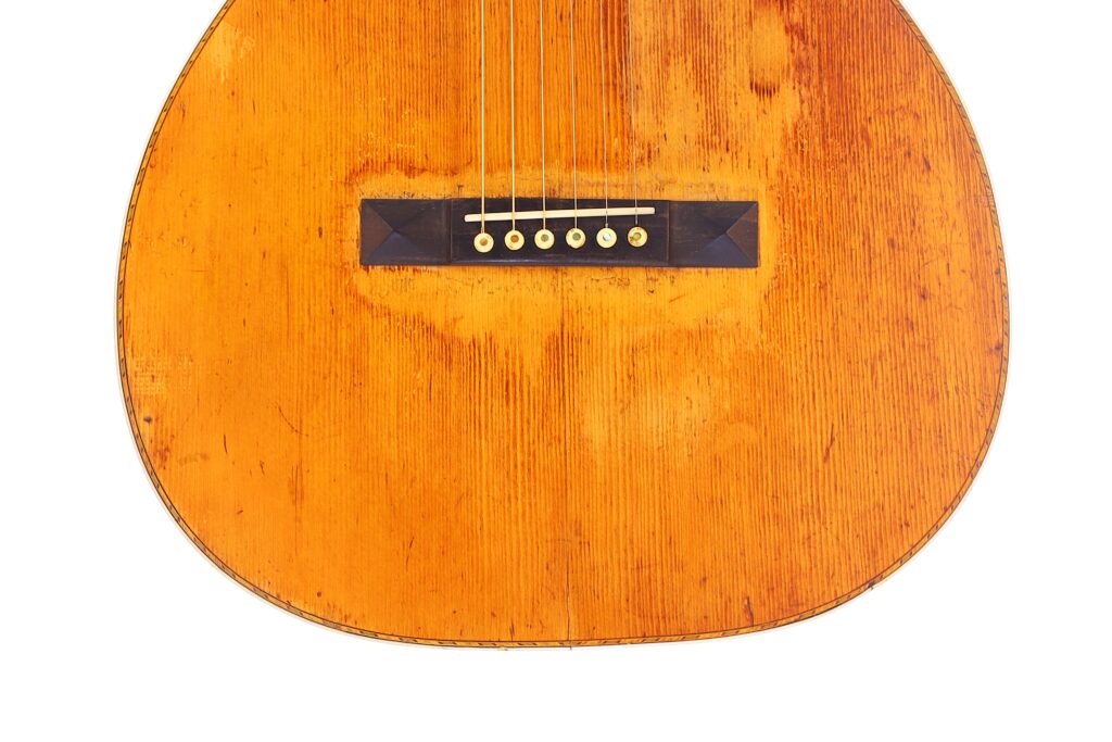 Nahaufnahme Der Unteren Hälfte Einer Martin 0-30 1917 Akustik-Gitarre, Wobei Der Abgenutzte Holzkorpus, Die Sechs Saiten Und Der Steg Vor Einem Weißen Hintergrund Für Einen Vintage-Look Hervorgehoben Werden.