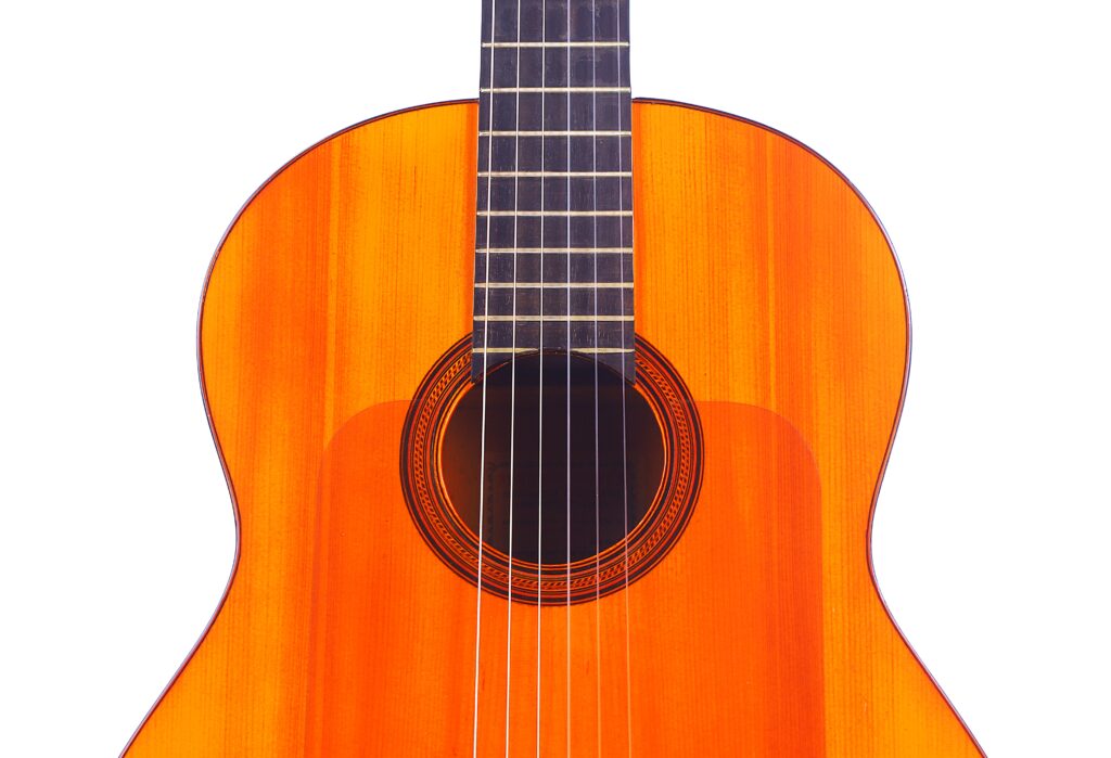 Nahaufnahme Von Korpus Und Hals Einer Flamenco-Gitarre Von Manuel Reyes Aus Dem Jahr 1955 Mit Leuchtend Orangefarbener Holzoberfläche, Die Das Schallloch, Die Saiten Und Das Griffbrett Vor Einem Weißen Hintergrund Hervorhebt.