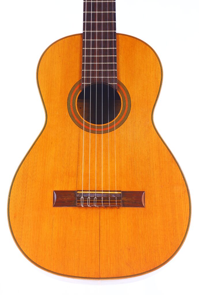 Eine Nahaufnahme Der Julián Gómez Ramírez 1933 Klassische Gitarre Zeigt Den Hölzernen Korpus, Die Saiten, Die Dekorativen Schalllochringe Und Einen Teil Des Griffbretts, Alles Vor Einem Weißen Hintergrund.