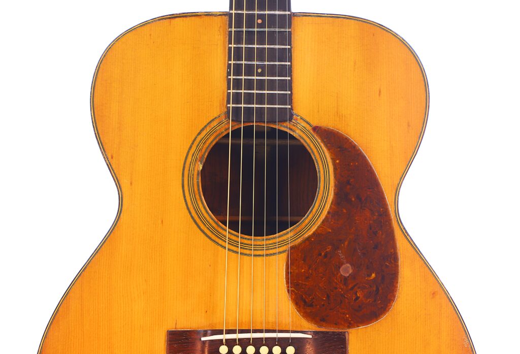 Nahaufnahme Einer Martin 000-21 Akustik Gitarre Von 1947 Mit Holzoberfläche, Sichtbaren Saiten, Schallloch Und Braunem Schildpatt-Schlagbrett. Die Gitarre Steht Aufrecht Vor Einem Weißen Hintergrund.