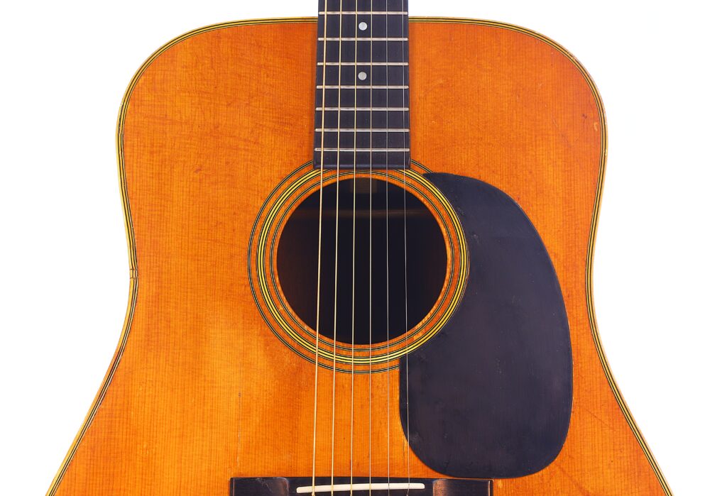 Nahaufnahme Des Korpus Einer Martin D-28 1971 Akustik Gitarre Mit Schallloch, Sechs Saiten, Schwarzem Schlagbrett Und Einem Teil Des Griffbretts Vor Einem Weißen Hintergrund.