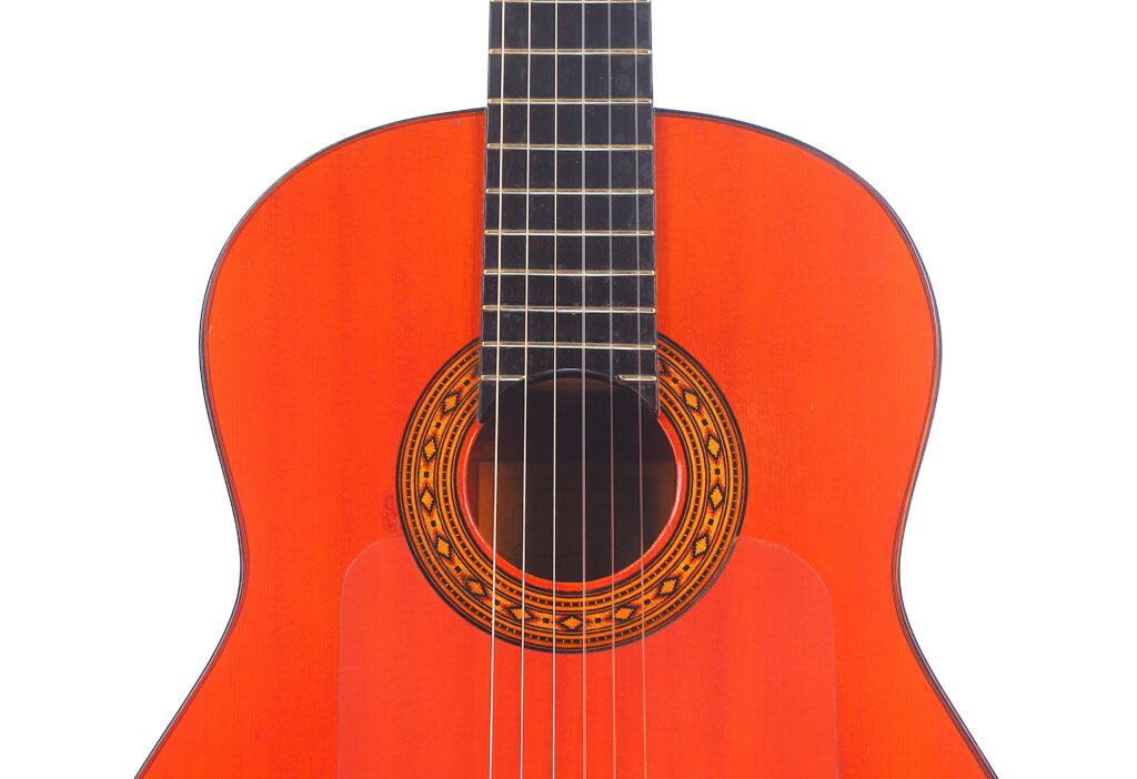 Nahaufnahme Des Oberen Korpus Einer Faustino Conde Flamenco-Gitarre Von Hermanos Conde Aus Dem Jahr 1983. Sie Hat Eine Leuchtend Rot-Orange Lackierung, Eine Dekorative Rosette Um Das Schallloch Und Sechs Saiten.