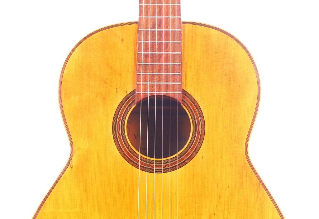 Eine Nahaufnahme Des Korpus Und Des Unteren Halses Der Vicente Tatay Alabau 1920 Klassische Gitarre, Wobei Die Saiten, Das Schallloch Und Die Hölzerne Oberfläche Vor Einem Weißen Hintergrund Hervorgehoben Werden.
