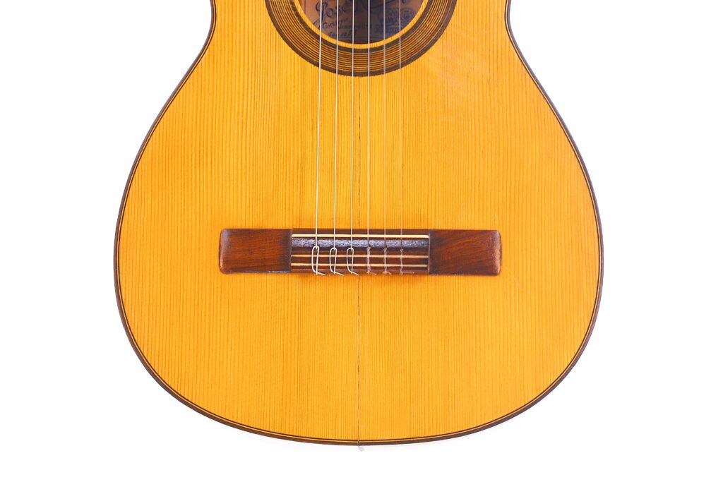 何塞-拉米雷斯(Jose Ramirez)1953 年创作的弗拉门戈吉他下半部分特写,白色背景下突出音孔、琴弦、木制琴桥和轻巧的琴身。.