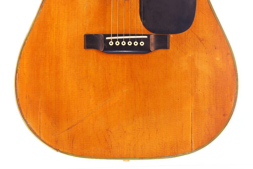 Nahaufnahme Des Korpus Der Martin D-28 1971 Akustik Gitarre, Wobei Die Holzoberfläche, Der Steg, Die Saiten Und Das Schwarze Schlagbrett Hervorgehoben Werden, Mit Sichtbaren Gebrauchsspuren Und Kratzern Auf Dem Holz.