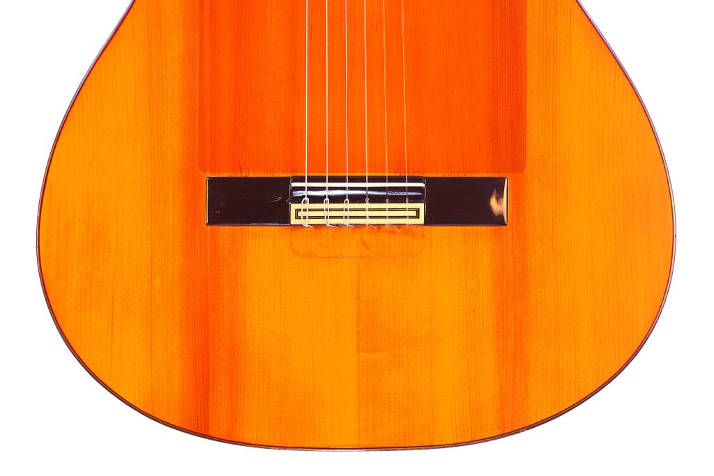 Nahaufnahme Der Unteren Hälfte Einer Flamenco-Gitarre Von Manuel Reyes Aus Dem Jahr 1955, Die Den Orange-Braunen Holzkorpus, Den Steg, Die Saiten Und Einen Teil Des Resonanzbodens Zeigt.