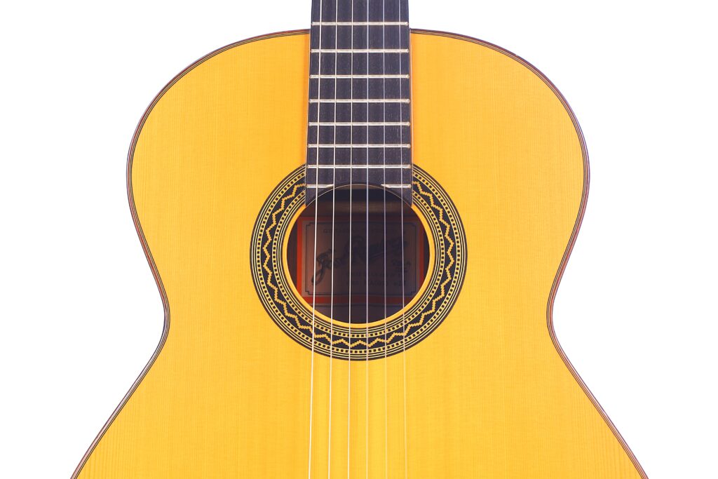 Nahaufnahme Von Korpus Und Hals Der José Ramírez Rb-A 636 Klassische Gitarre. Hervorzuheben Sind Die Saiten, Die Dekorative Rosette Um Das Schallloch Und Die Helle Holzoberfläche Vor Weißem Hintergrund.