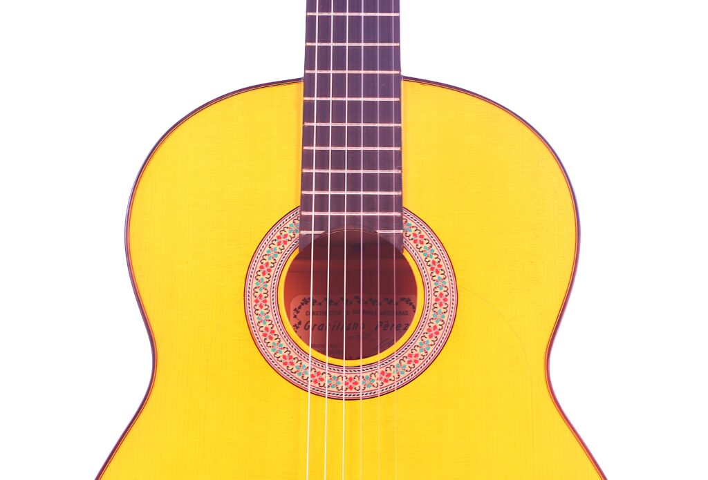 Nahaufnahme Des Korpus Und Der Saiten Der Graciliano Perez 2025 Flamenco-Gitarre. Hervorzuheben Sind Die Dekorative Rosette Um Das Schallloch Und Die Leuchtend Gelbe Lackierung, Die Auf Weißem Hintergrund Gezeigt Wird.