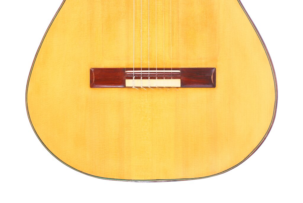 Nahaufnahme Des Unteren Teils Der Oscar Orozco 2023 Santos Hernández Flamenco-Gitarre, Wobei Der Helle Holzkorpus, Die Saiten Und Der Dunkle Holzsteg Vor Einem Weißen Hintergrund Hervorgehoben Werden.