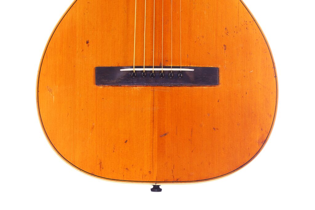 Nahaufnahme Des Korpus Der Washburn 1894 Parlor Akustik Gitarre Mit Sechs Saiten, Einem Dunklen Holzsteg Und Einer Hellbraunen Holzoberfläche Mit Sichtbarer Maserung Und Kleinen Kratzern.