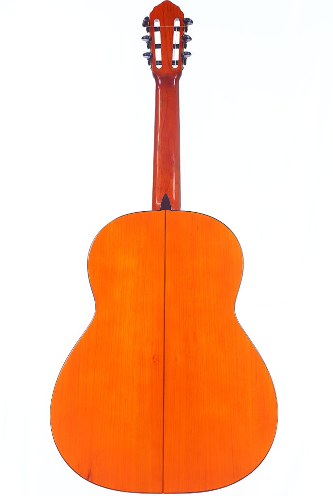 Rückansicht Der Manuel Reyes 1955 Flamenco-Gitarre. Sie Hat Eine Glänzende Orangefarbene Holzoberfläche, Sechs Wirbel Und Einen Geteilten Boden Mit Einer Sichtbaren Dunklen Mittelnaht.