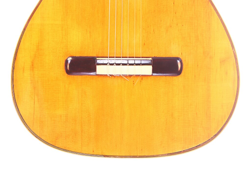 Nahaufnahme Von Korpus Und Steg Einer Vicente Tatay Alabau 1920 Klassische Gitarre Mit Sechs Saiten Und Einer Holzoberfläche Vor Weißem Hintergrund.