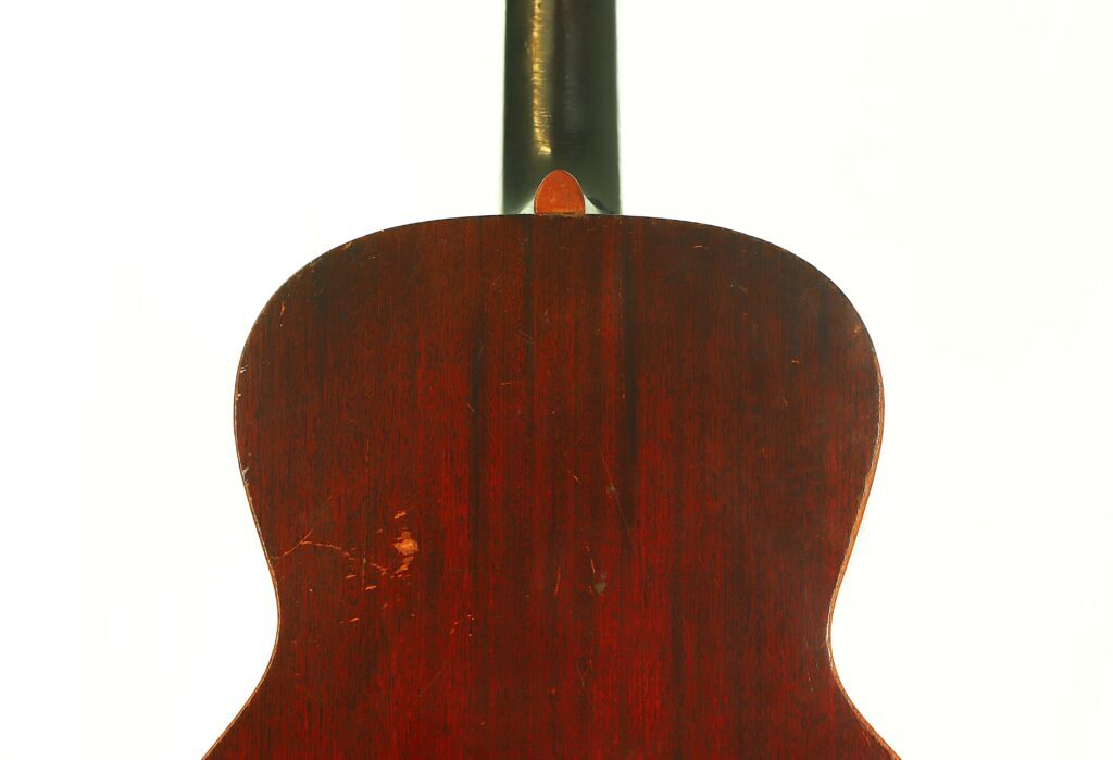 Nahaufnahme Der Rückseite Einer Gibson L-00 1934 Akustikgitarre Mit Dunkler Holzoberfläche, Die Einige Kratzer Und Abnutzungserscheinungen Aufweist, Vor Einem Schlichten Weißen Hintergrund.