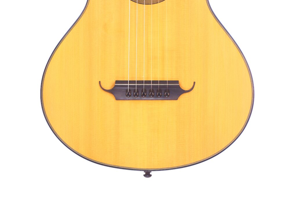 Nahaufnahme Der Unteren Hälfte Einer Grobert Romantikgitarre 2016 Von Yoann Charbonnier Mit Sechs Saiten, Holzsteg Und Hellem Korpus Vor Weißem Hintergrund.