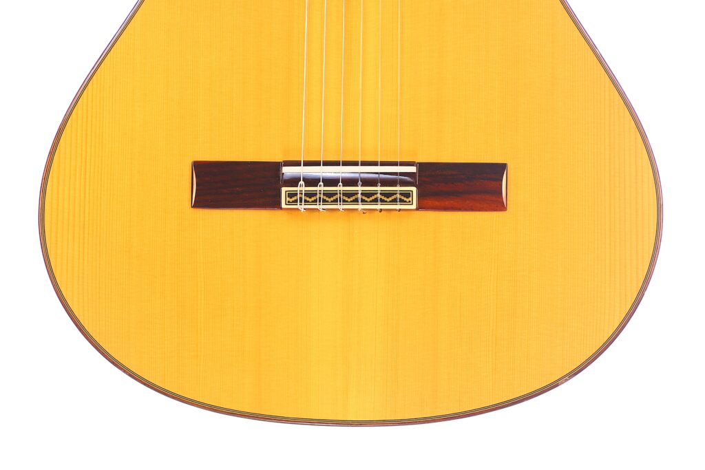 Nahaufnahme Der Unteren Hälfte Der José Ramírez Rb-A 636 Klassische Gitarre. Hervorzuheben Sind Die Saiten, Der Holzsteg Und Der Helle Korpus Vor Einem Weißen Hintergrund.