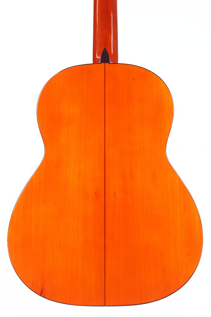 Eine Nahaufnahme Der Rückseite Einer Flamenco-Gitarre Von Manuel Reyes Aus Dem Jahr 1955 Zeigt Die Glänzende Orangefarbene Holzoberfläche, Die Vertikale Mittelnaht Und Die Glatte, Geschwungene Form Vor Einem Weißen Hintergrund.