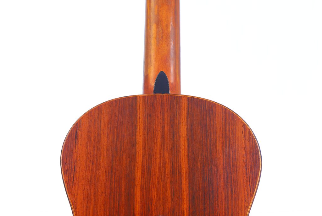 Nahaufnahme Der Rückseite Und Des Halses Einer Lester Devoe 1996 Negra Flamenco-Gitarre, Die Aus Poliertem Holz Gefertigt Ist Und Deren Natürliche Maserung Und Textur Vor Einem Schlichten Weißen Hintergrund Hervorgehoben Wird.