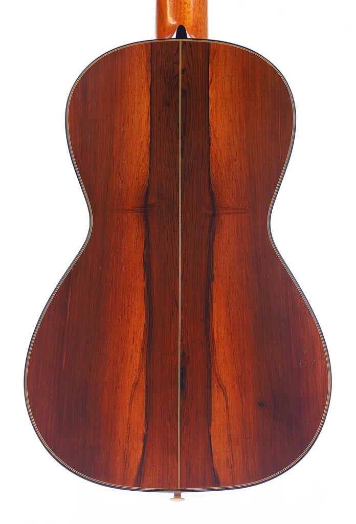 베른하르트 크레세 1999 파노르모 로맨틱 기타의 뒷면은 흰색 바탕에 중앙 이음새와 짙은 나뭇결이 있는 광택이 나는 적갈색 목재로 제작되었습니다.