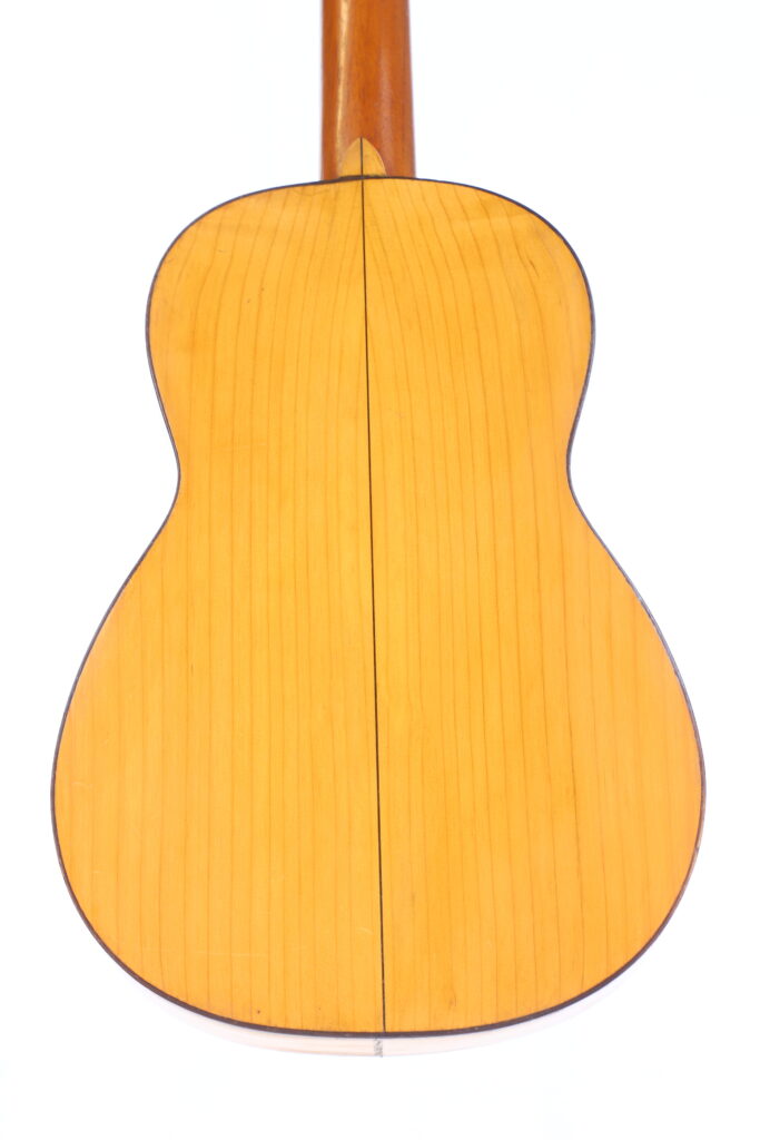 图中展示的是何塞-拉米雷斯 1953 年制作的弗拉门戈吉他的背面,木质表面较浅,纹理清晰可见,形状对称,中间有一条深色竖线。.