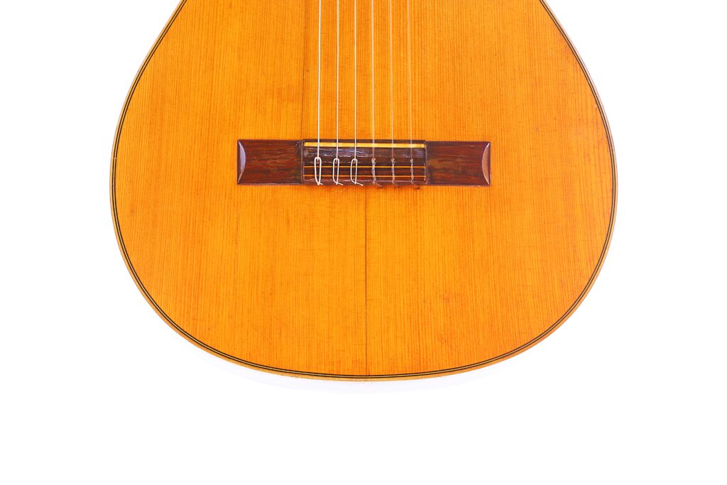 Nahaufnahme Der Unteren Hälfte Einer Klassischen Gitarre Von Julián Gómez Ramírez Aus Dem Jahr 1933 Vor Weißem Hintergrund, Wobei Der Holzkorpus, Die Saiten Und Der Steg Hervorgehoben Werden.