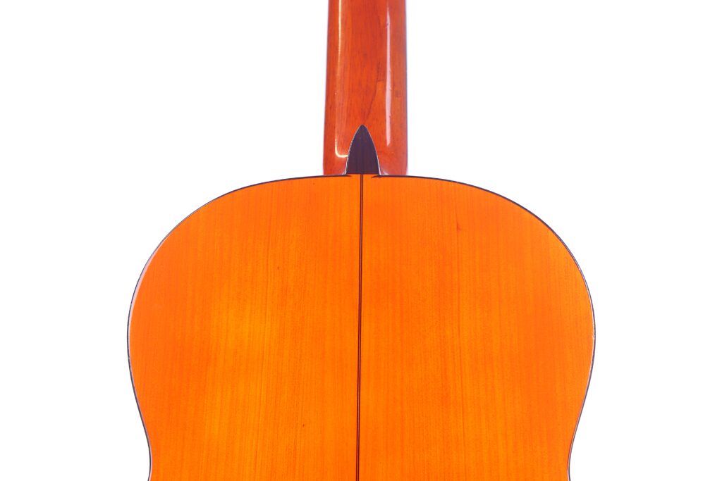 Die Abbildung Zeigt Die Rückseite Einer Flamenco-Gitarre Von Manuel Reyes Aus Dem Jahr 1955 Mit Einer Hellbraunen, Polierten Holzoberfläche, Die Teilweise Den Hals Und Den Korpus Mit Einer Zentralen Naht Vor Einem Weißen Hintergrund Zeigt.