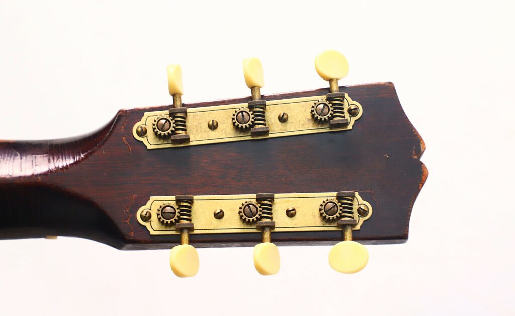 Nahaufnahme Der Rückseite Einer Gibson L-00 1934 Akustikgitarre Mit Zwei Metallstimmplatten Mit Zahnrädern Und Sechs Cremefarbenen Stiftwirbeln Vor Einem Schlichten Weißen Hintergrund.