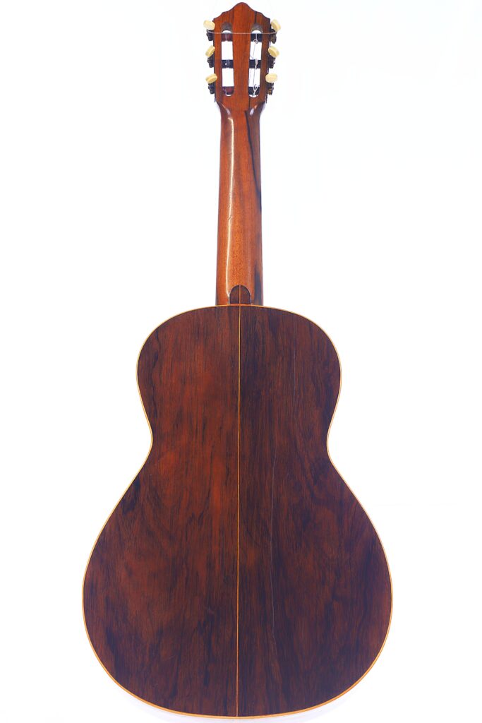 Das Bild Zeigt Die Rückseite Einer Julián Gómez Ramírez 1933 Klassische Gitarre, Die Eine Polierte Dunkle Holzoberfläche Mit Einer Zentralen Vertikalen Naht Aufweist. Der Hals Der Gitarre Und Die Stimmwirbel Sind Ebenfalls Sichtbar.