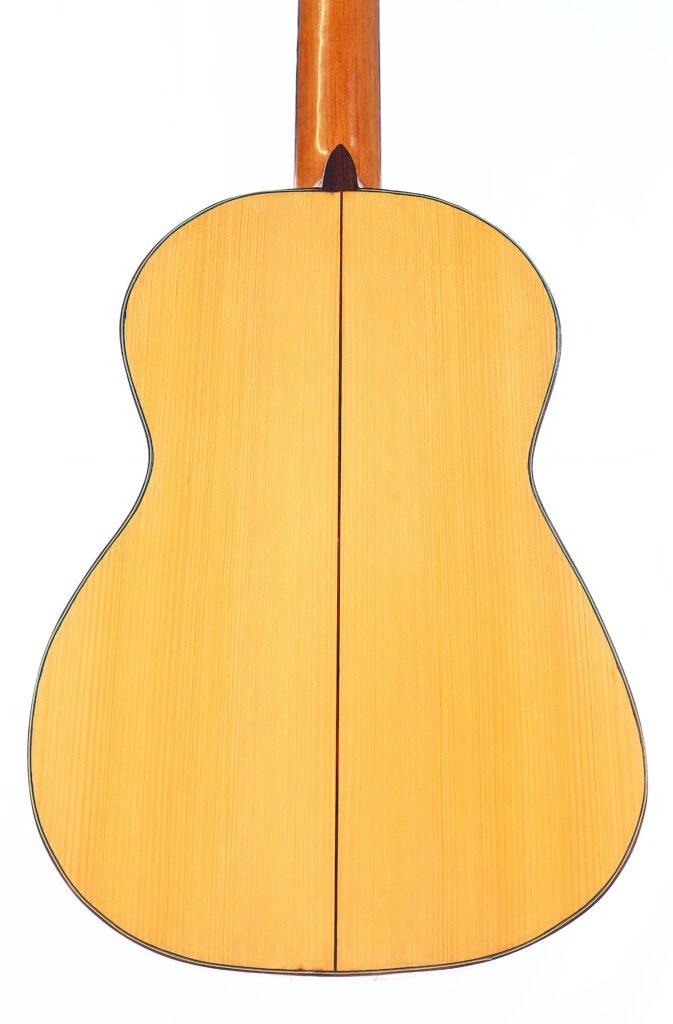 Das Bild Zeigt Die Rückseite Einer Oscar Orozco 2023 Santos Hernández Flamenco-Gitarre Mit Einer Hellen Holzoberfläche, Einer Dunklen Mittelnaht Und Einem Braunen Hals. Der Umriss Der Gitarre Hebt Sich Deutlich Von Dem Weißen Hintergrund Ab.