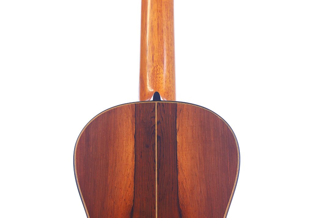 사진은 베른하르트 크레세 1999 파노르모 로맨틱 기타의 뒷모습을 보여줍니다. 광택이 나는 목재 바디와 뒷면 중앙에 이음새가 있는 넥이 평범한 흰색 배경 앞에 서 있어 강조됩니다.