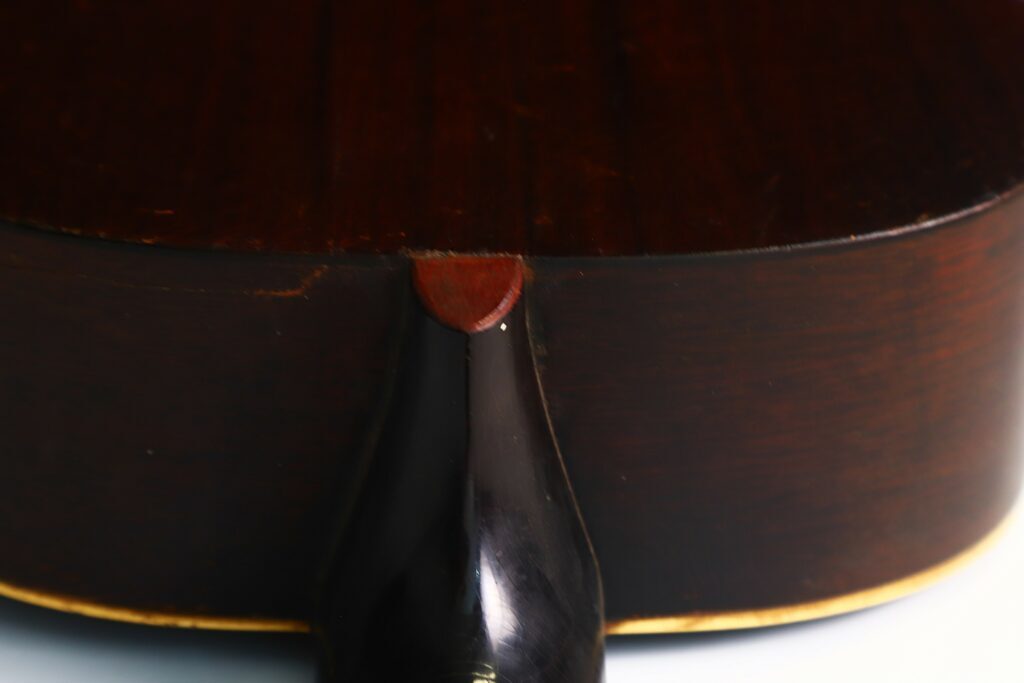 Nahaufnahme Der Halsverbindung, Wo Der Schwarze Hals Auf Den Dunkelbraunen Holzkorpus Einer Gibson L-00 1934 Akustik Gitarre Trifft, Wobei Die Maserung Und Das Finish Hervorgehoben Werden.