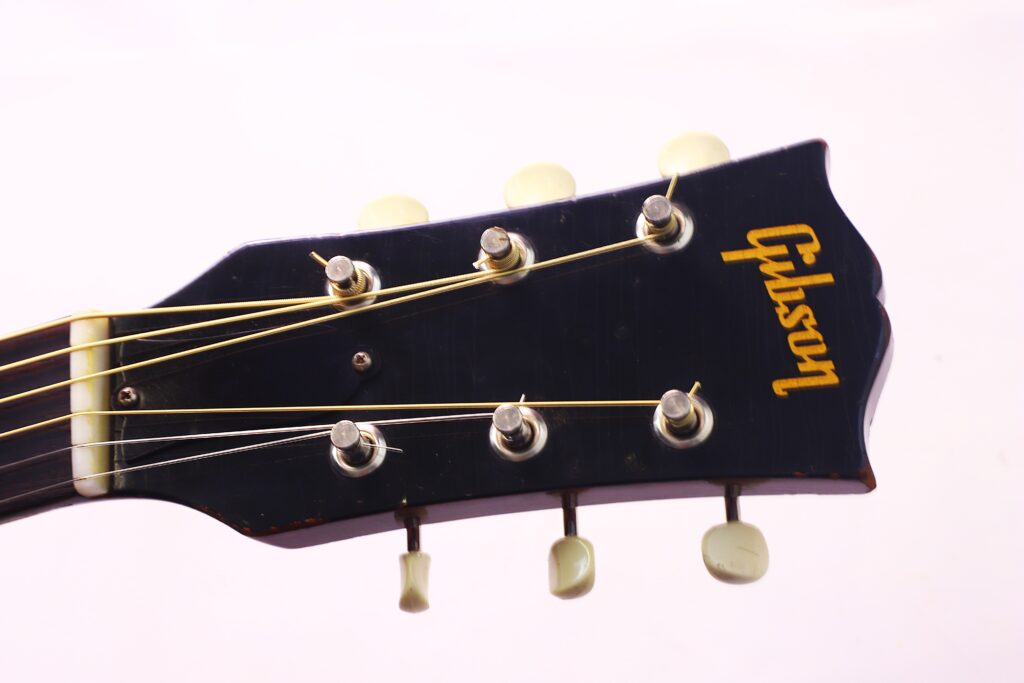 Nahaufnahme Der Schwarzen Kopfplatte Der Gibson J-45 1962 Akustik Gitarre Mit Sechs Stimmwirbeln Und Einem Goldenen Gibson-Logo Auf Weißem Grund.