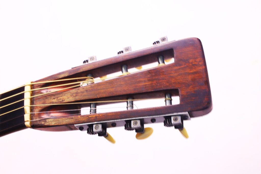 Nahaufnahme Der Kopfplatte Der Martin 0-30 1917 Akustik Gitarre, Die Drei Stimmwirbel, Eine Holzoberfläche Und Nylonsaiten Vor Einem Schlichten Weißen Hintergrund Zeigt.