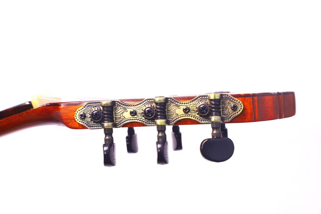 Nahaufnahme Der Kopfplatte Einer Manuel Reyes 1955 Flamenco-Gitarre Mit Verschnörkelten Metallstimmwirbeln Und Einer Holzoberfläche, Isoliert Auf Weißem Hintergrund.