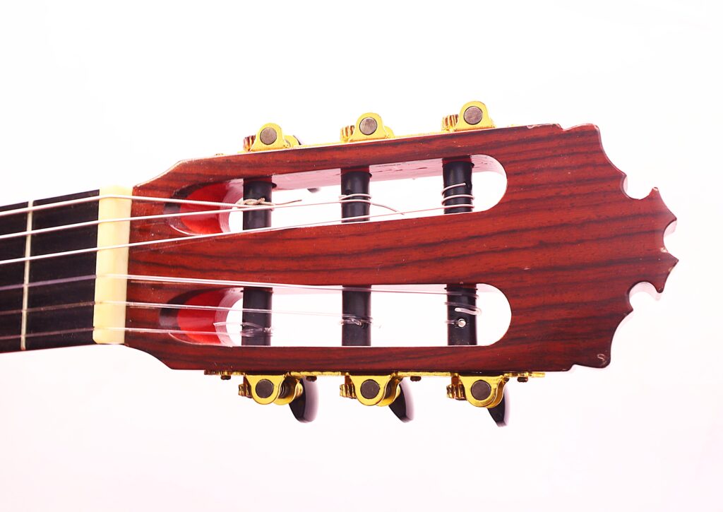 Nahaufnahme Der Kopfplatte Der Manuel Guillena 2017 Blanca Flamenco-Gitarre Mit Sechs Goldfarbenen Stimmwirbeln, Nylonsaiten Und Einer Holzoberfläche Auf Weißem Hintergrund.