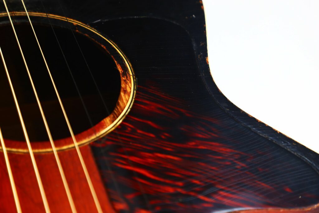 Eine Nahaufnahme Der Gibson L-00 1934 Akustik Gitarre Zeigt Das Schallloch, Die Saiten Und Ein Dunkles, Rötlich-Schwarzes Holzmaserungsmuster Auf Weißem Hintergrund.