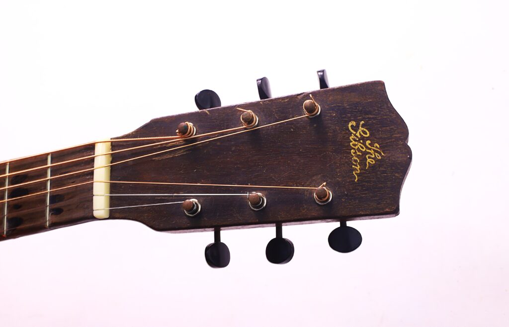 Nahaufnahme Der Kopfplatte Mit Stimmwirbeln Und Saiten, Mit Dem Gibson L-1 1926 Akustik Gitarre Logo In Gold Auf Dunklem Holz - Eine Anspielung Auf Das Klassische Akustikgitarren-Design.