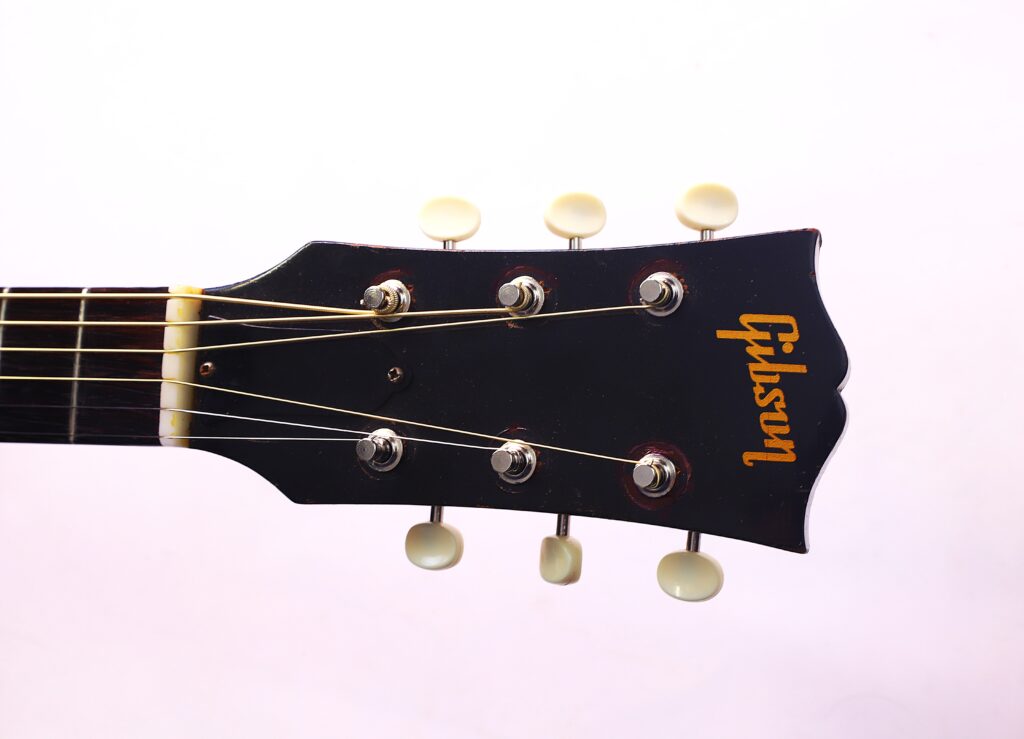 Nahaufnahme Der Schwarzen Kopfplatte Einer Gibson J-45 1957 Akustik-Gitarre Mit Sechs Stimmwirbeln Und Einem Gelben Gibson-Logo Vor Weißem Hintergrund.