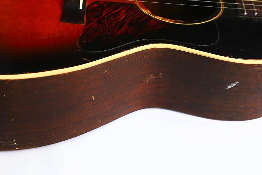 Nahaufnahme Der Seite Einer Gibson L-00 1934 Akustik Gitarre, Die Die Holzmaserung, Ein Paar Kratzer Und Einen Teil Des Gitarrenkorpus Vor Einem Weißen Hintergrund Zeigt.