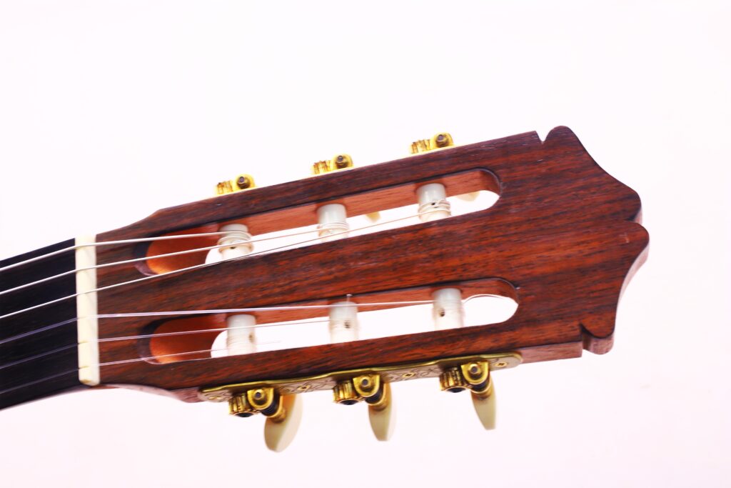 Nahaufnahme Der Kopfplatte Der Oscar Orozco 2023 Santos Hernández Flamenco-Gitarre Mit Sechs Saiten, Goldenen Wirbeln Und Einer Dunklen Holzoberfläche Vor Einem Schlichten Weißen Hintergrund.