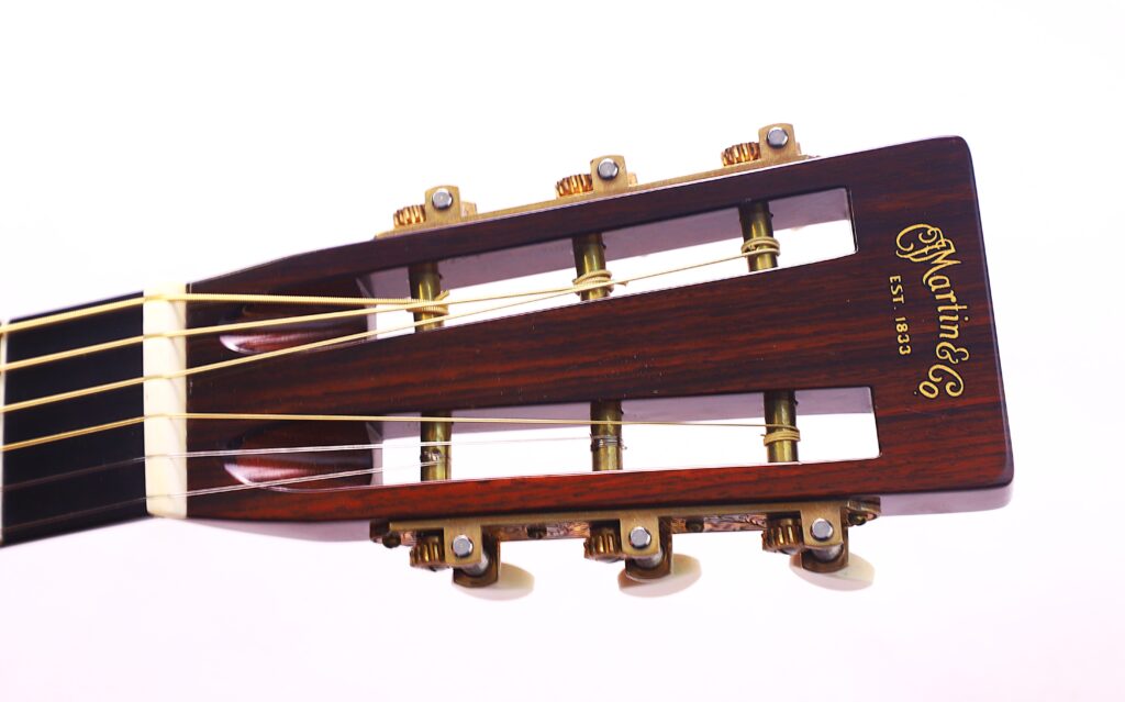 Nahaufnahme Der Kopfplatte Einer Martin 0-28 Ian Anderson Akustik Gitarre, Mit Goldenen Stimmwirbeln, Cremefarbenen Knöpfen, Nylonsaiten Und Dem Martin-Logo Auf Dunklem Holz Vor Weißem Hintergrund.