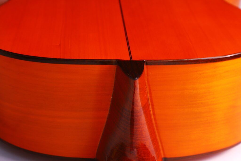 Nahaufnahme Des Bodens Und Des Halses Der Manuel Reyes 1955 Flamenco Gitarre, Wobei Die Polierte Holzmaserung Und Die Warme Orange-Braune Lackierung Hervorgehoben Werden.