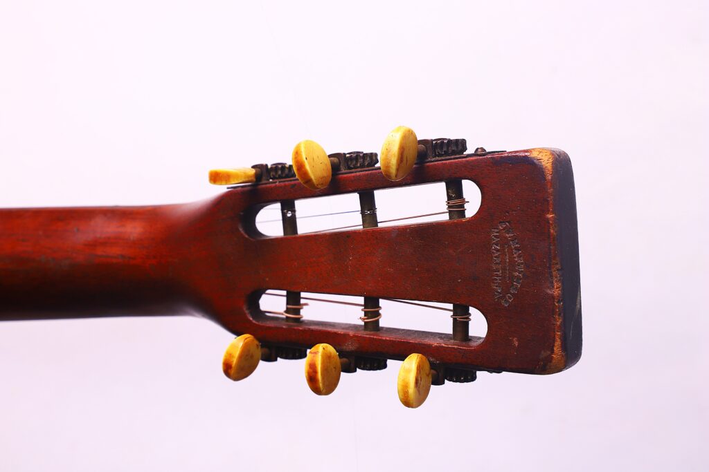 Close-Up Of The Headstock Of A Martin 00-18 1922 Akustik Gitarre, Showing Six Yellow Tuning Pegs Against A Plain Light Background.